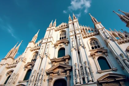 Vue en contre-plongée de la façade gothique du Dôme de Milan avec ses flèches en marbre blanc se découpant sur un ciel bleu profond