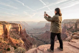 Femme photographiant le Grand Canyon avec un smartphone depuis un promontoire de grès en Utah, paysage désertique américain en arrière-plan